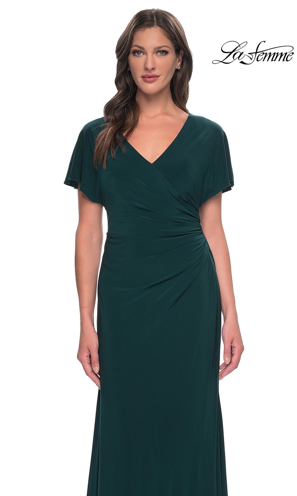 A woman wearing a dark green, V-neck La Femme 29997 formal dress with a sheath skirt and short, draped sleeves.